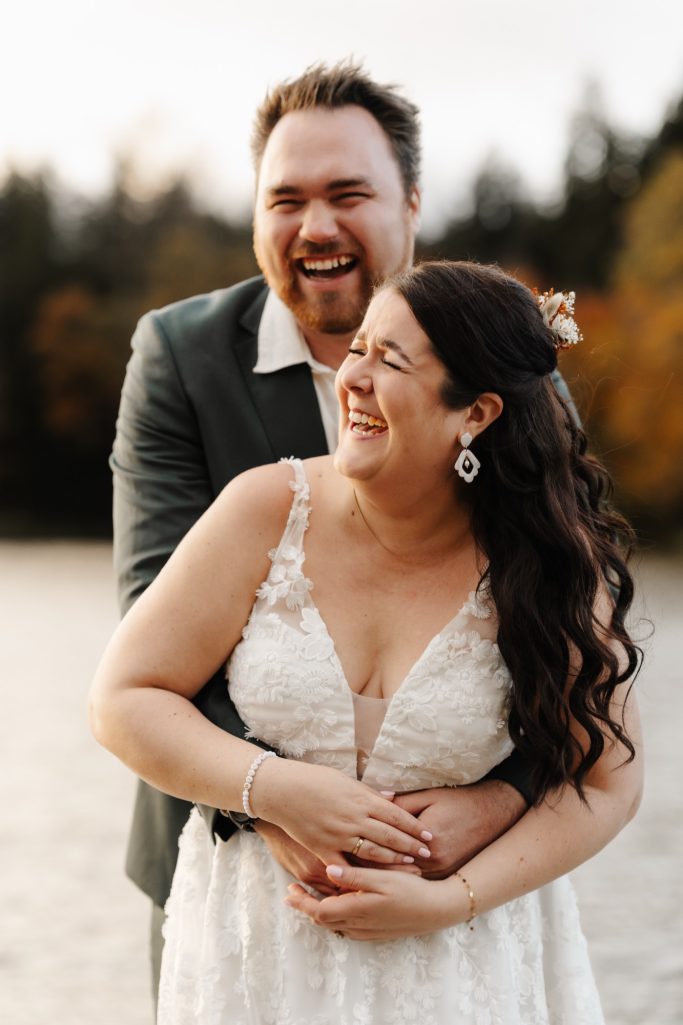 Paar in romantischer Umarmung am Wasser, beide lachen und glücklich.