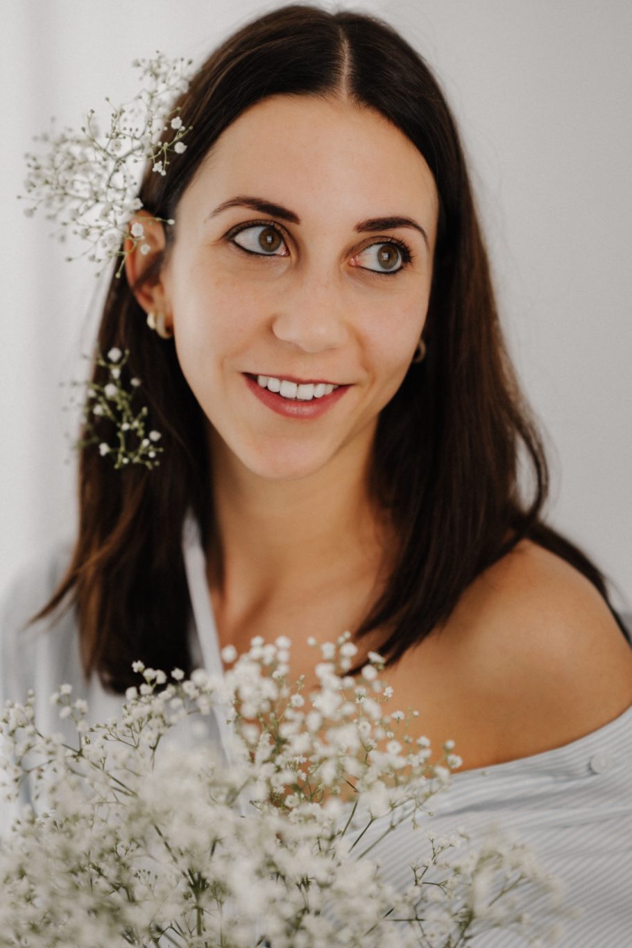 Porträt einer Frau mit langen, braunen Haaren, die mit weißen Blumen arrangiert ist.