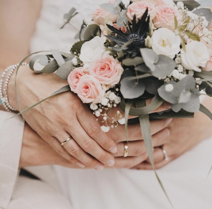 Braut hält einen Blumengesteck mit rosa und weißen Rosen sowie grünen Blättern.