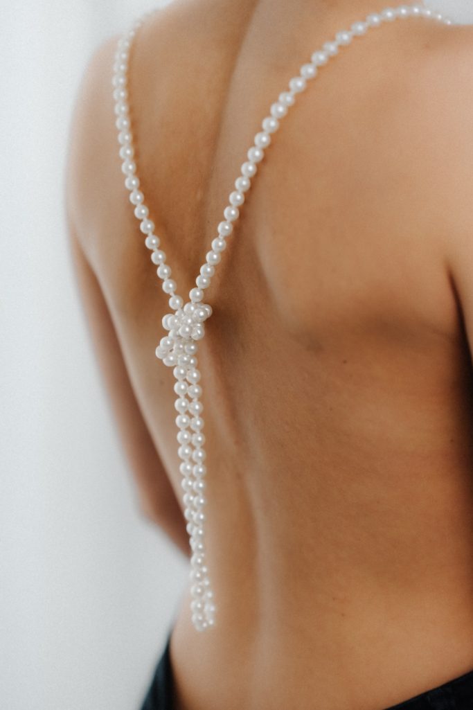 Eine nackte Rückenansicht mit einer Perlenkette und dekorativem Anhänger.